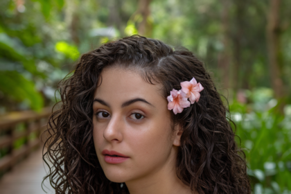 Woman with natural summer curly hairstyle adorned with a floral hair accessory in a lush, green outdoor environment